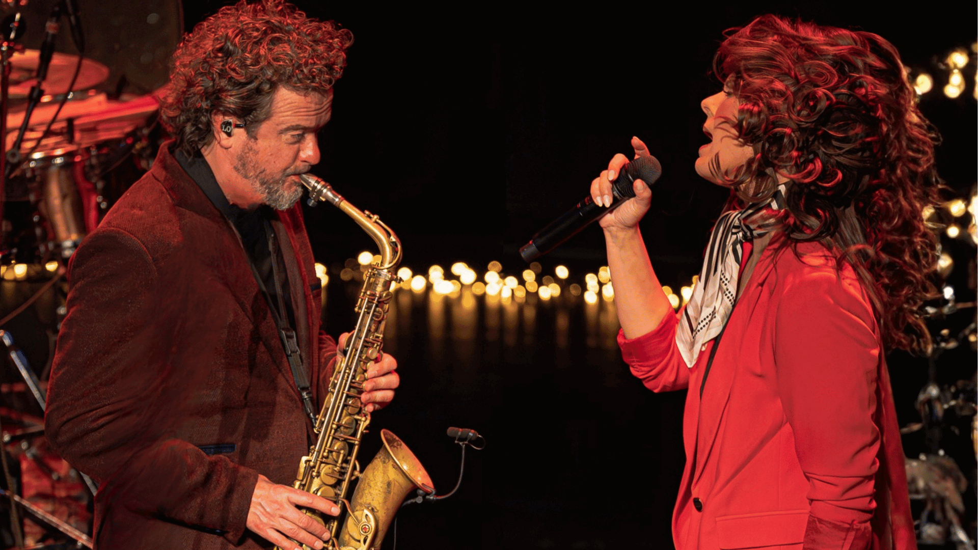 twee artiesten. een met saxofoon en de ander zingend met een microfoon. ze staan tegenover elkaar