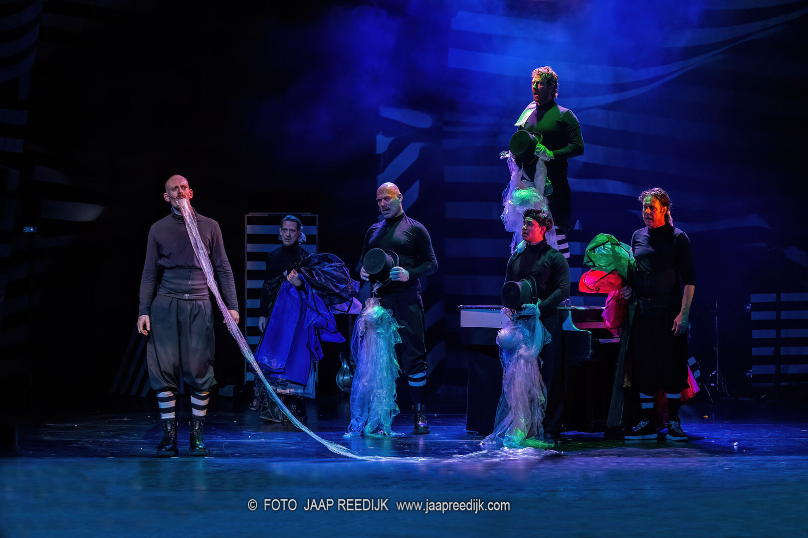 Actors performing on stage during a theatrical production with colorful lighting and elaborate costumes.
