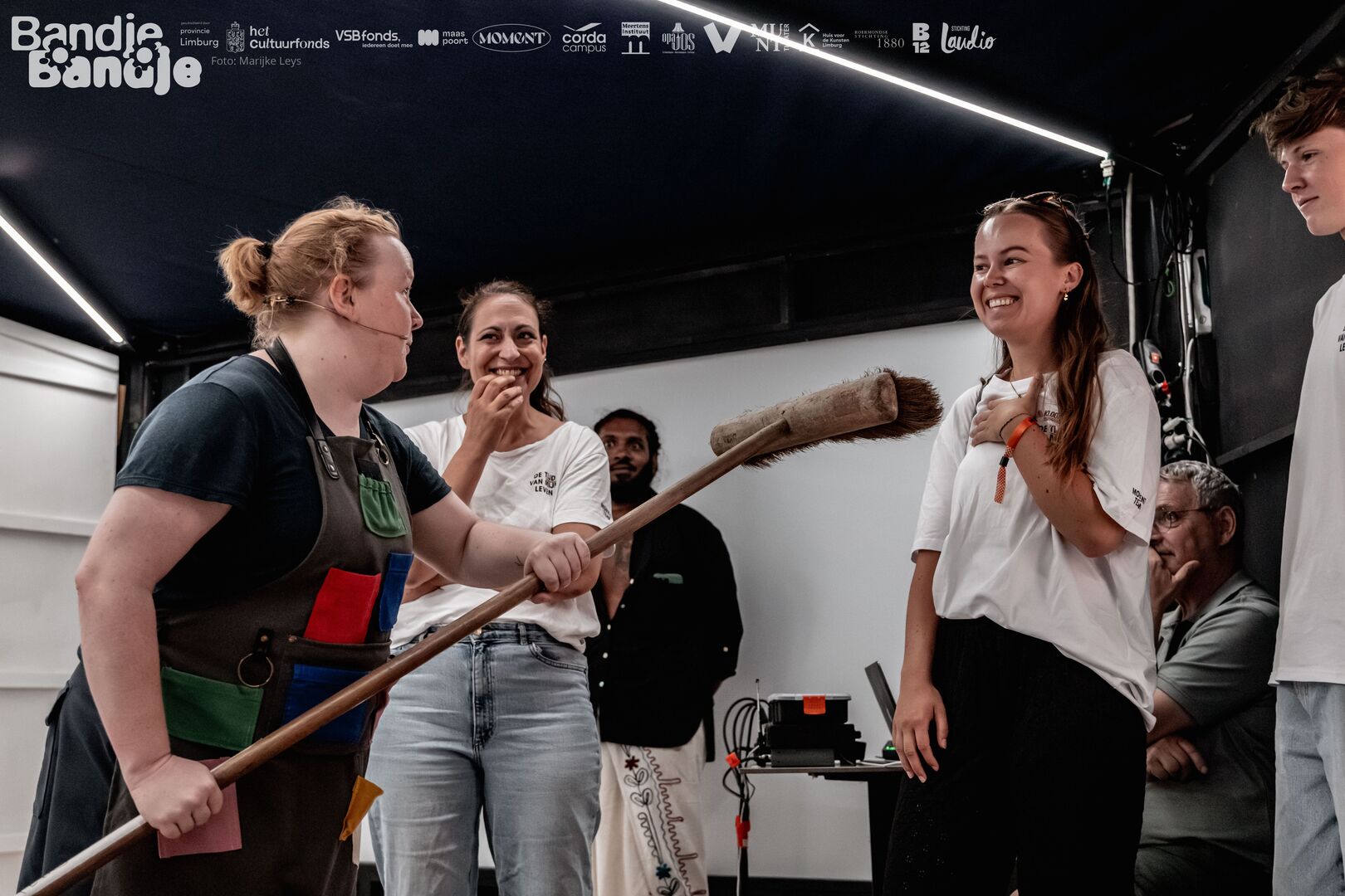 Actrice met bezem gericht op drie bezoekers