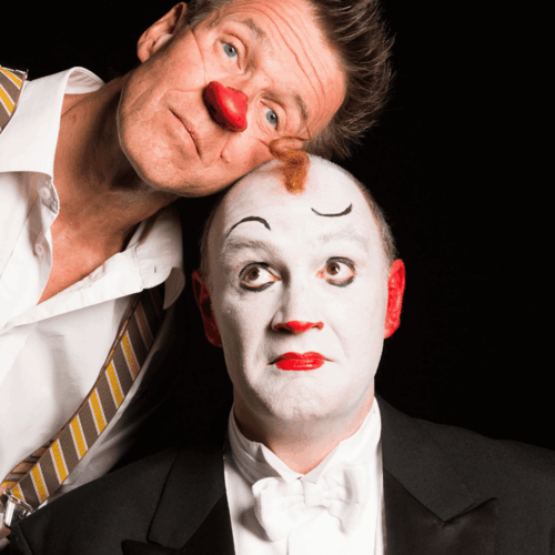 Twee clowns met opvallende schmink en kostuums poseren samen, de ene met een rode neus en de andere met een strik.