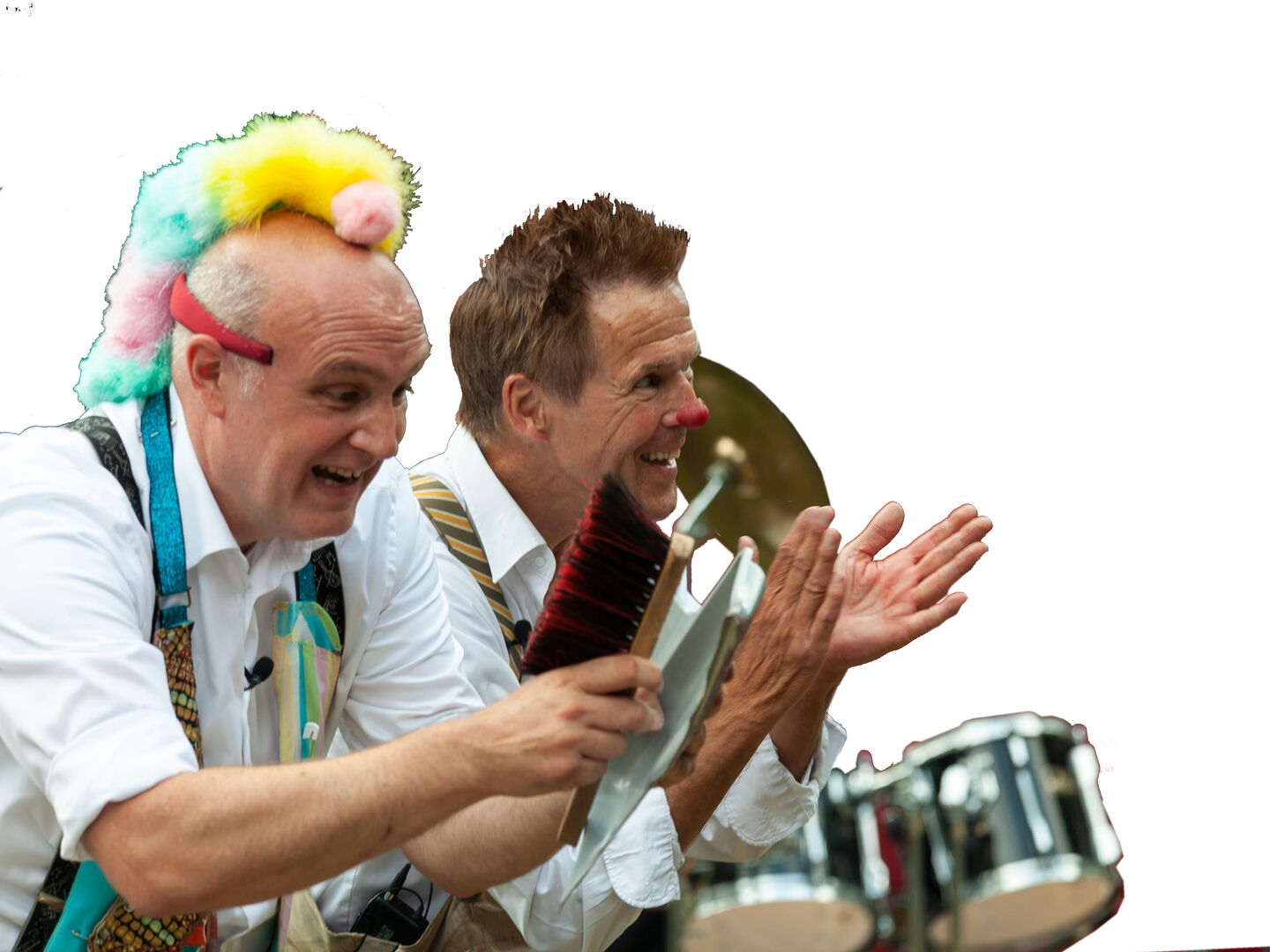 Twee mannen in kleurrijke kostuums spelen op muziekinstrumenten en klappen enthousiast in een feestelijke setting.