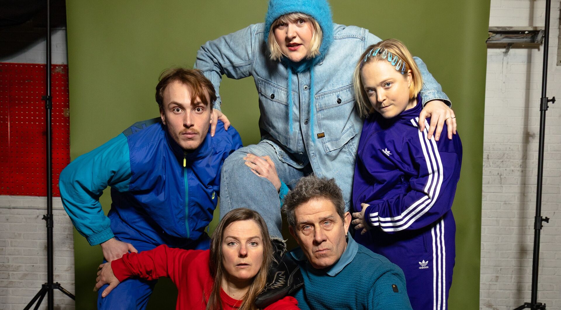 Vijf mensen poseren in kleurrijke sportoutfits tegen een groene achtergrond in een creatieve fotoshoot.