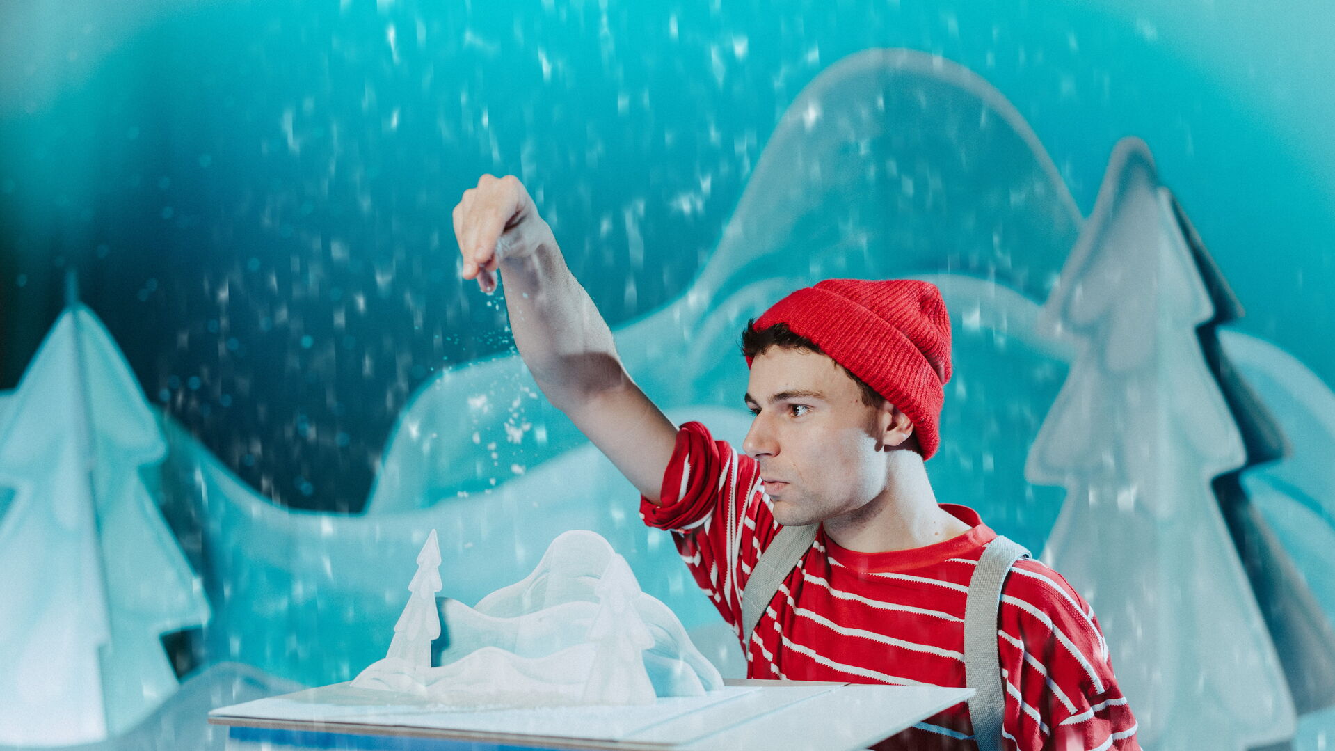 Jonge man in rode muts en gestreept shirt, die een sneeuwlandschap creëert in een speelse winterse setting.