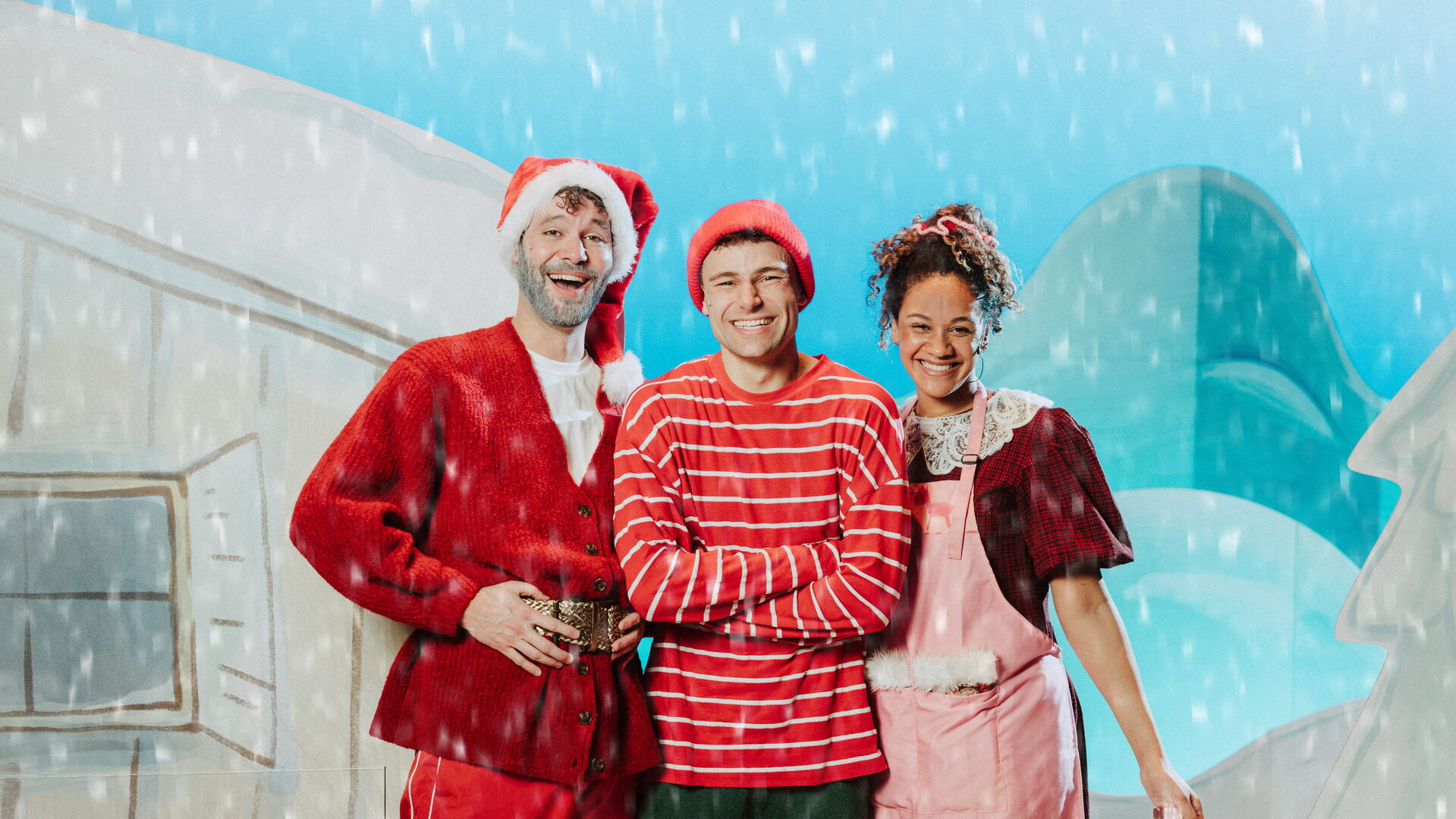 Drie mensen in feestelijke kerstoutfits staan voor een sneeuwachtige achtergrond, glimlachend naar de camera.