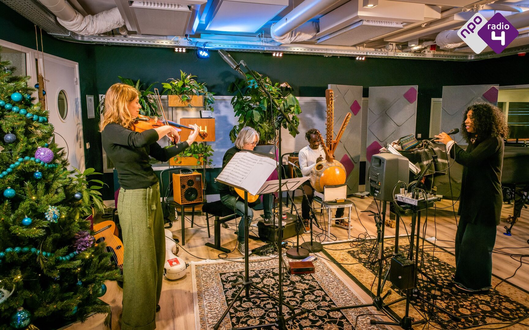 Groep muzikanten speelt in een sfeervolle ruimte, omringd door planten en kerstdecoratie.