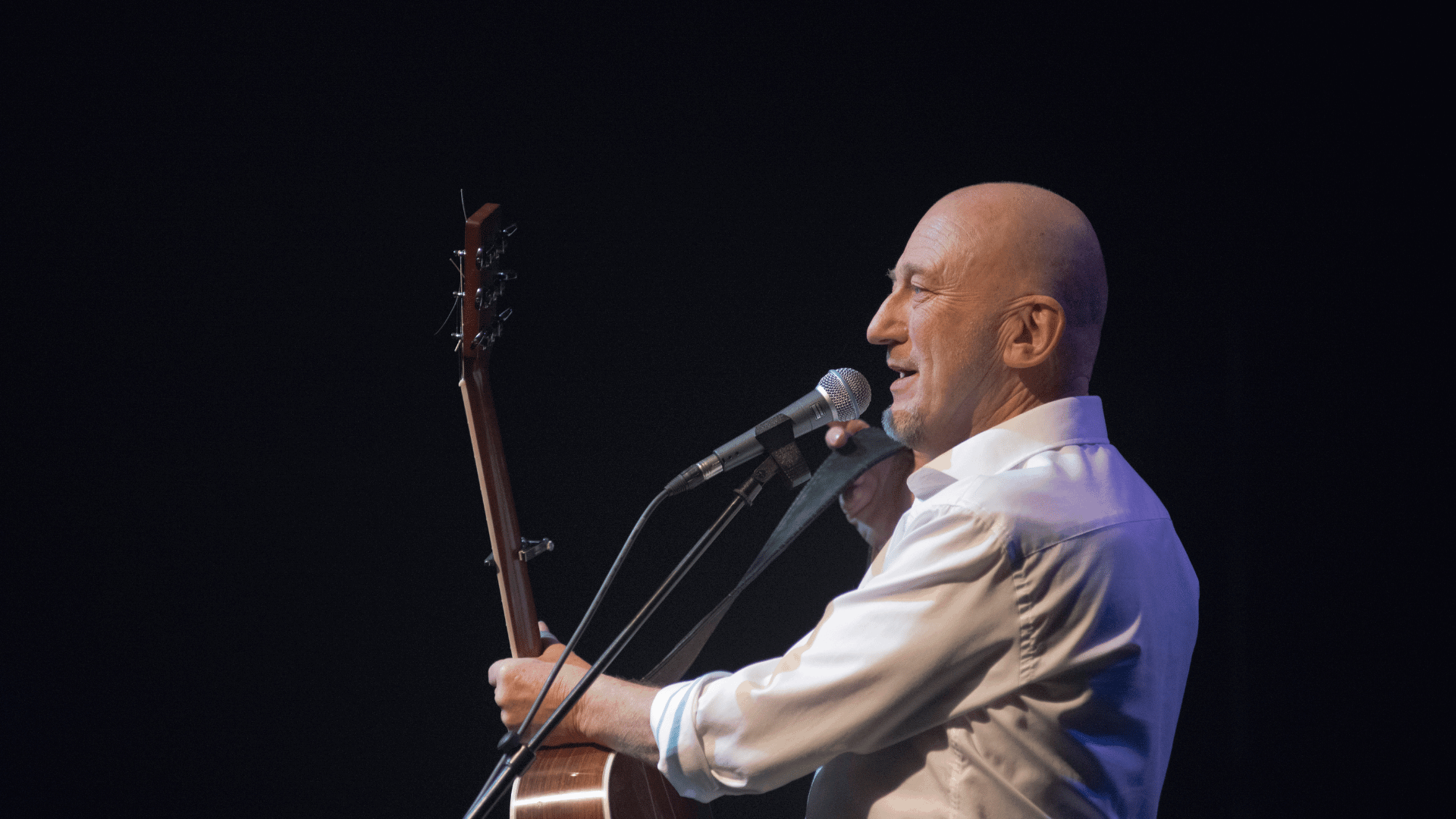 Gerard van Maasakker achter microfoon met gitaar in zijn hand