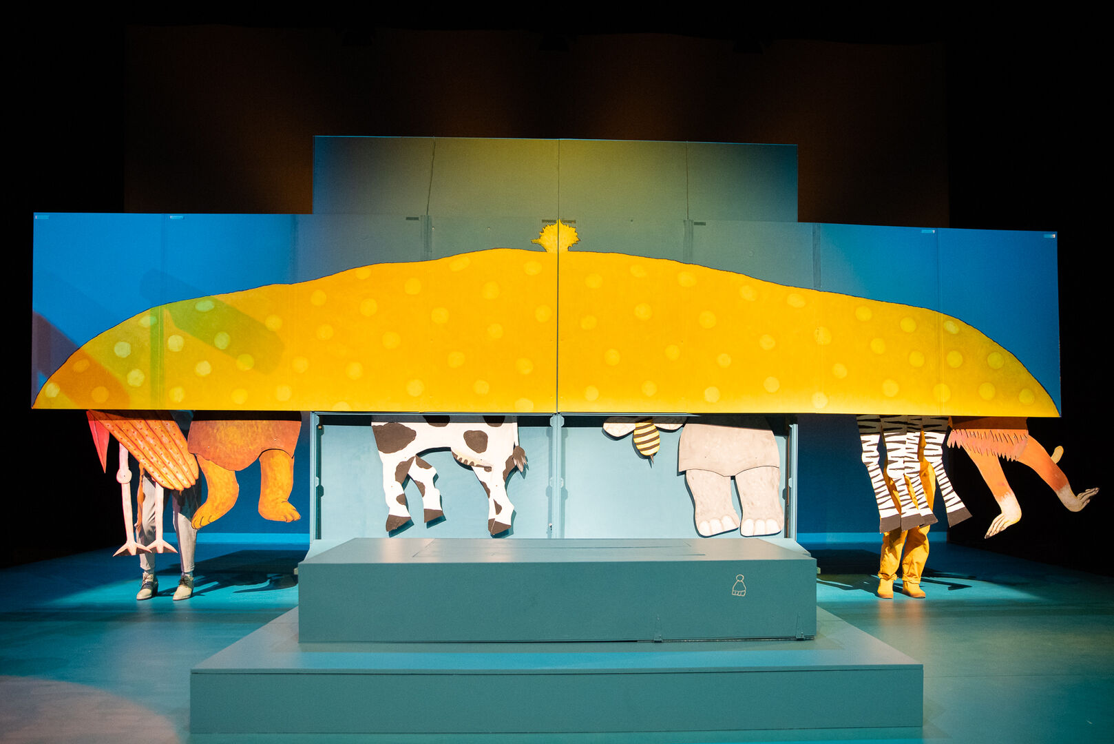 Theaterdecor met grote, kleurrijke afbeeldingen van dieren en een zonsondergang, gebruikt voor een kindervoorstelling.