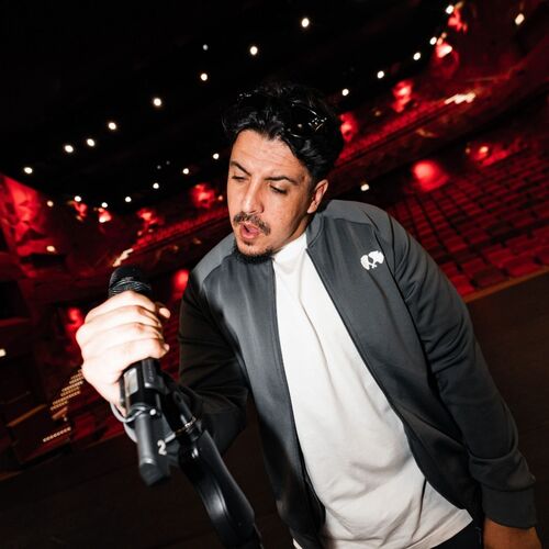 Man met een microfoon op een podium in een theater met rode lichten op de achtergrond.