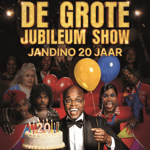 Jandino met ballonnen en een taart in zijn hand, zittend in een theaterzaal met allemaal andere spelers om hem heen