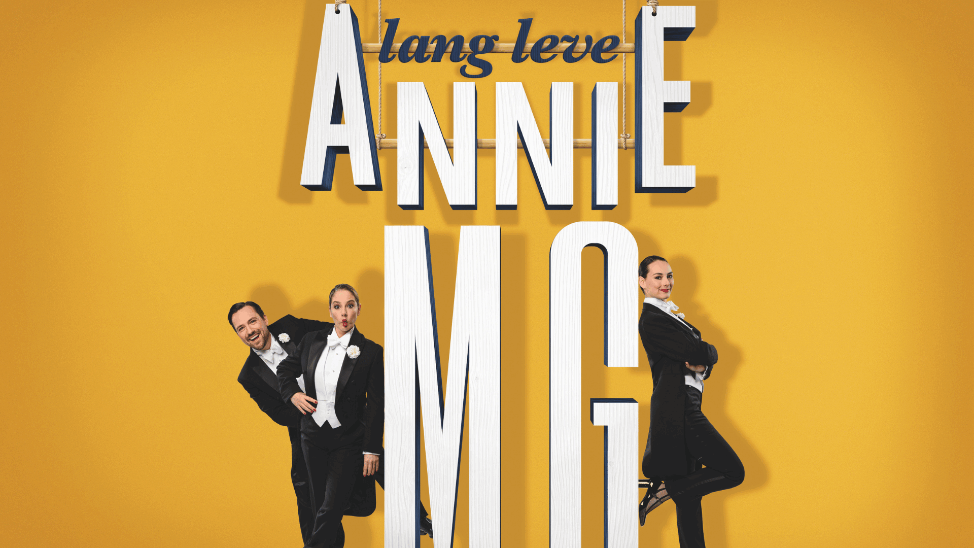lang leve Annie MG in witte letters voor gele achtergrond en 3 mensen in pak erom heen