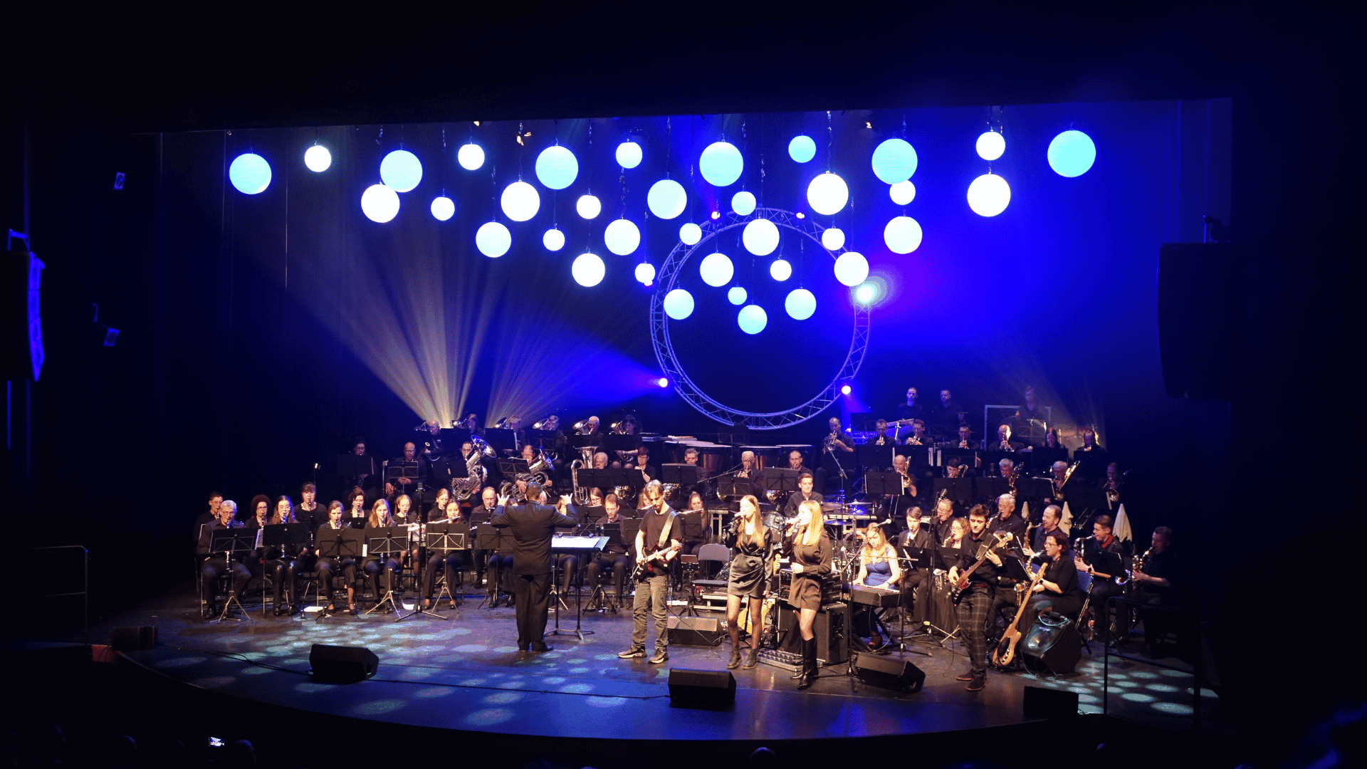 podium gevuld met verschillende mensen met instrumenten en dirigent