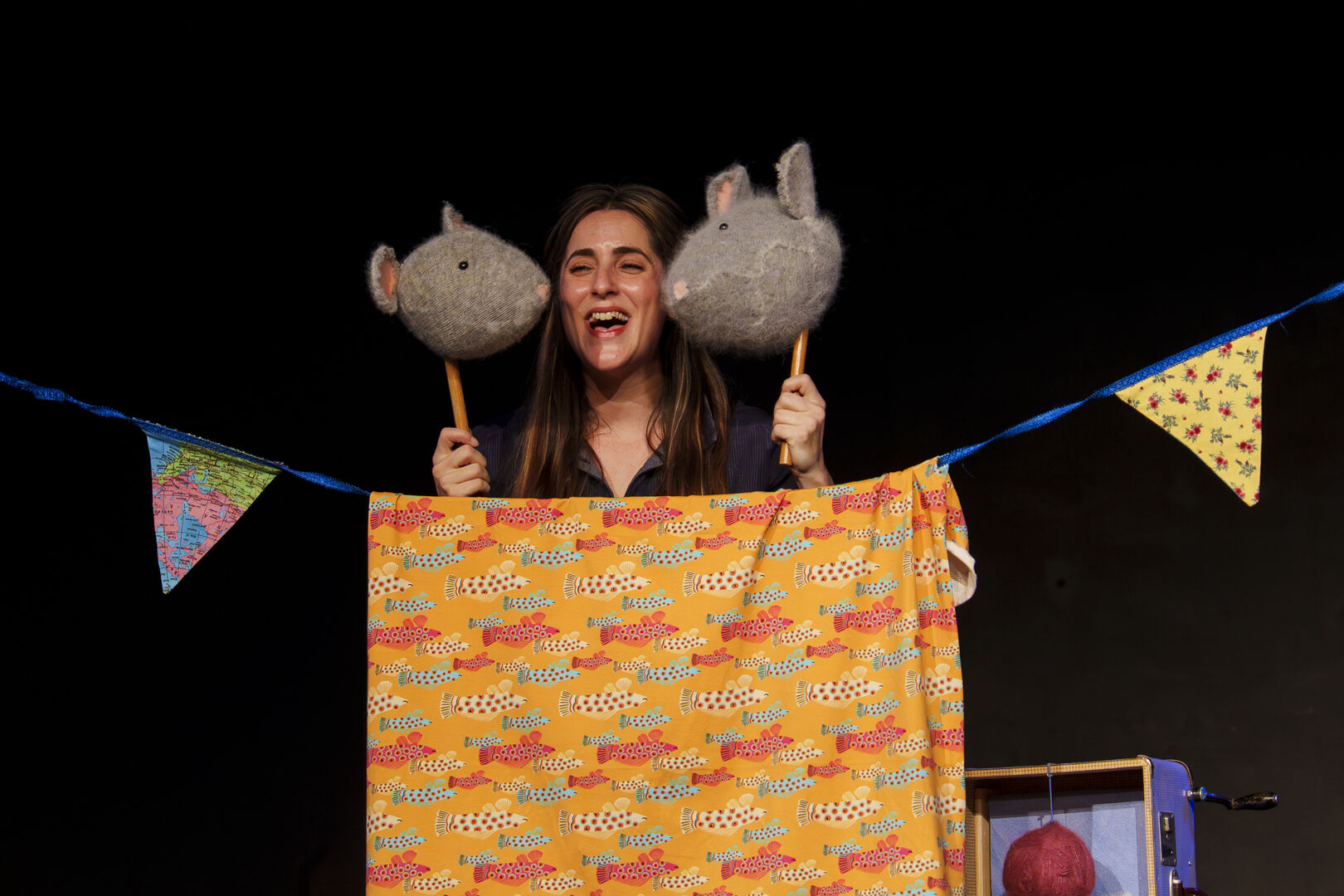 Vrouw met puppets van een olifant en een konijn achter een kleurige scherm in een theatersetting.