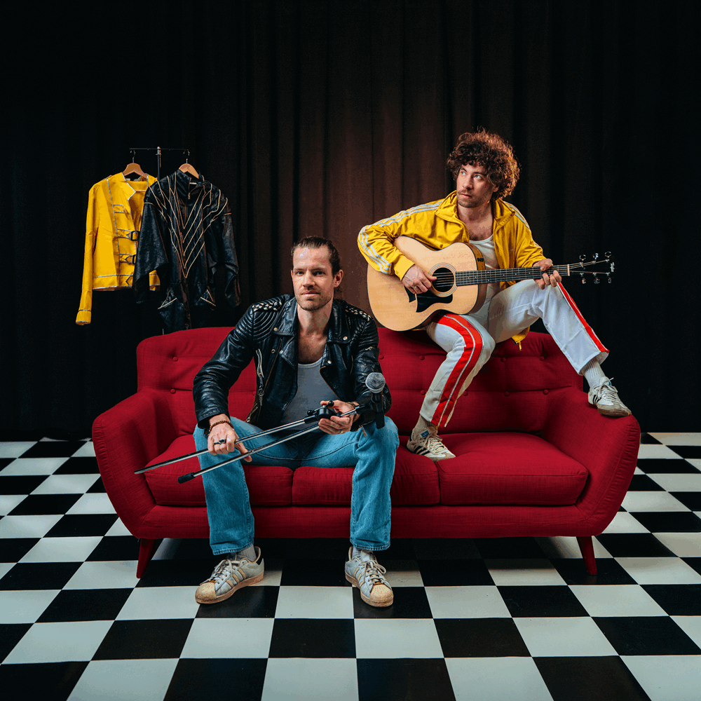 2 mannen op rode bank, een zit op de leuning met een gitaar