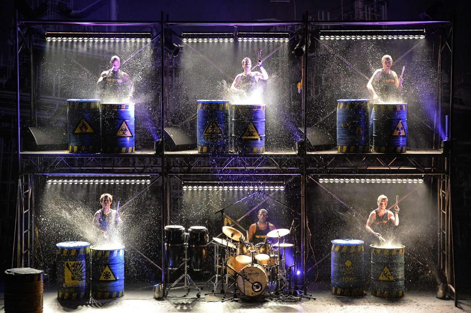 Zes muzikanten spelen op vaten, verlicht door krachtige verlichting, met een drummer in het midden.
