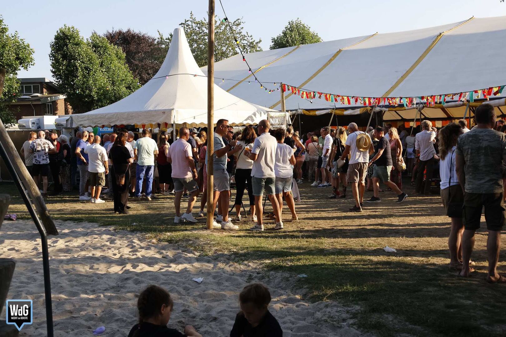Een druk bezochte buitenfeestlocatie met een grote tent en mensen die dansen en socializen.